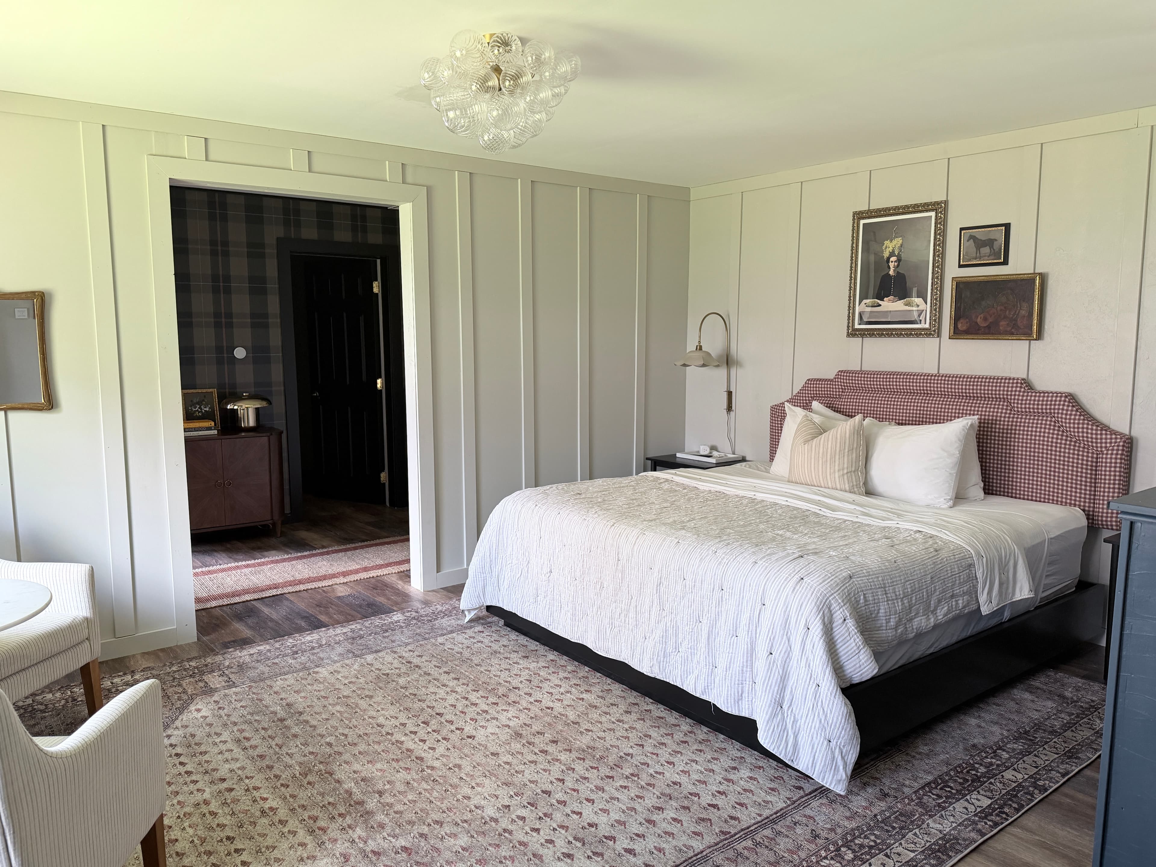 A cozy, well-decorated bedroom featuring a large bed, patterned rug, and an adjoining room.