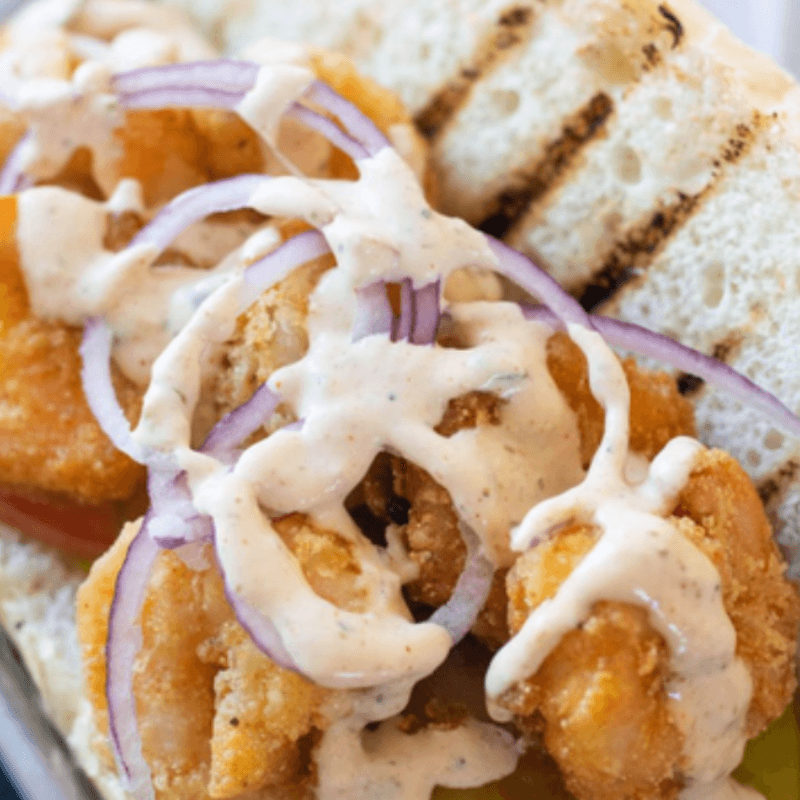 A close-up of crispy shrimp drizzled with sauce and garnished with sliced red onions on toasted bread.