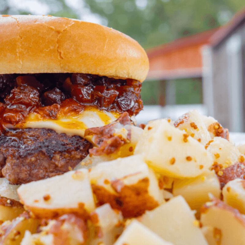 A close-up of a juicy hamburger topped with sauce and cheese, accompanied by seasoned diced potatoes.