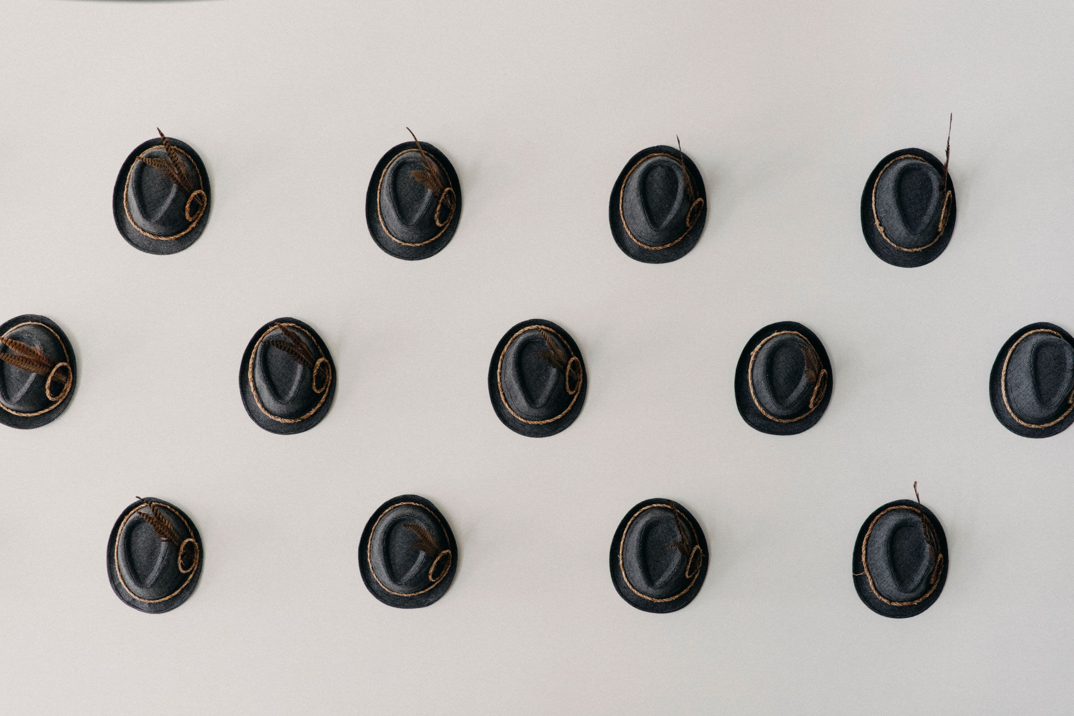 A symmetrical arrangement of small black hats displayed on a light wall.