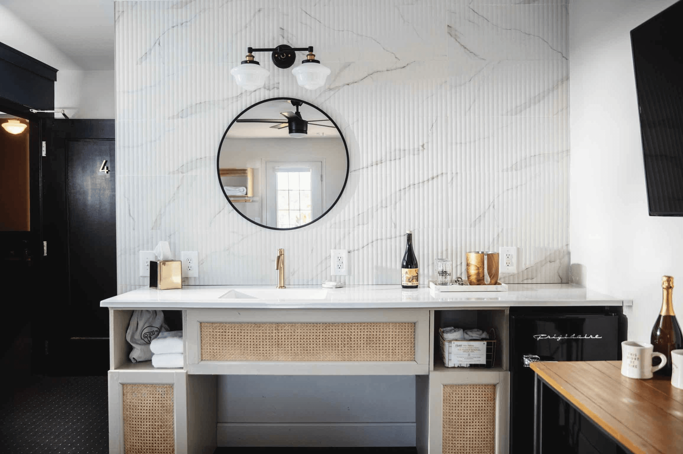 Modern bathroom vanity with a round mirror, minimalist decor, and a mini fridge.