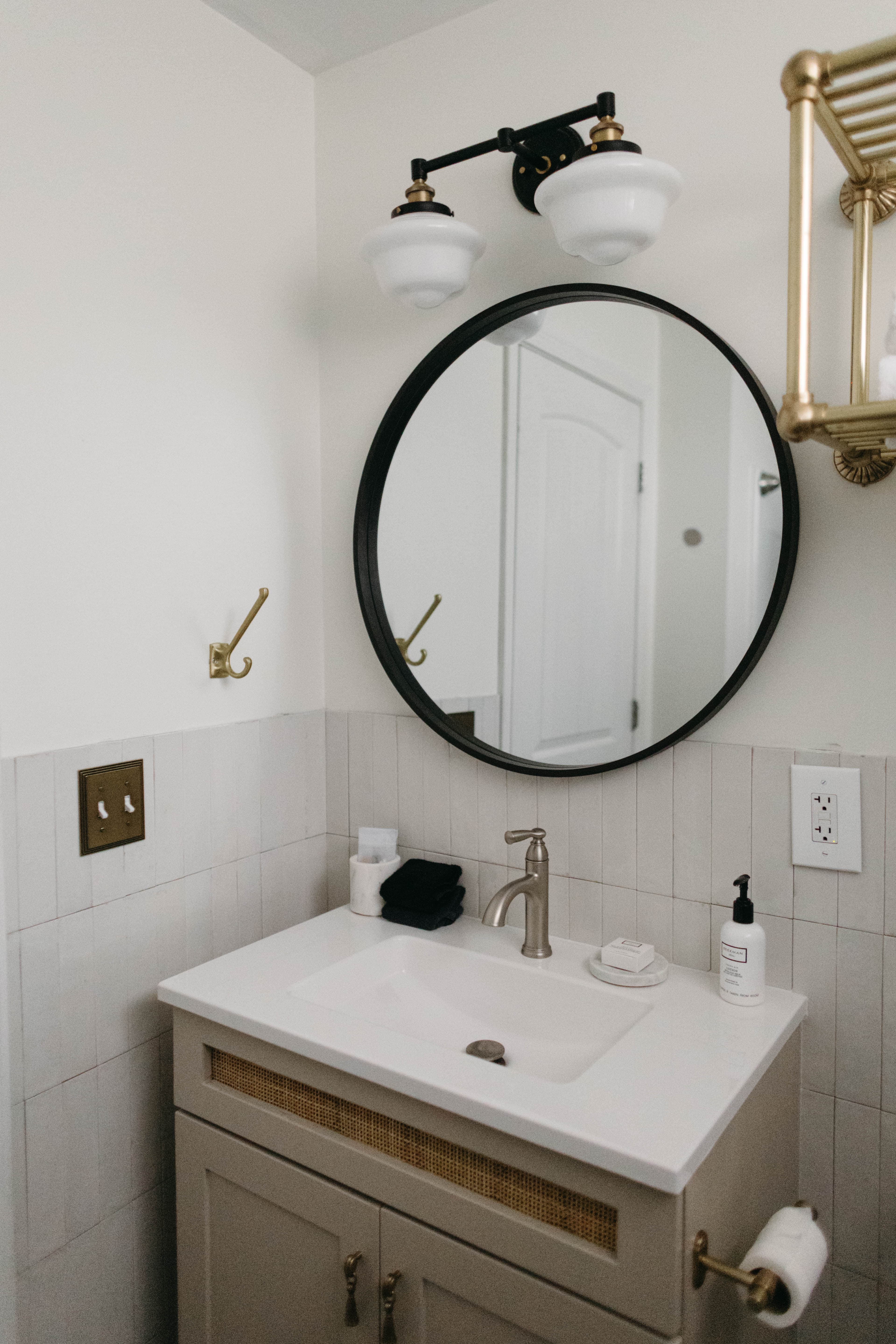 A modern bathroom with a round mirror above a sink, featuring gold accents and white fixtures.