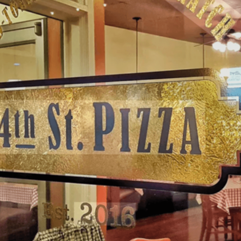Sign for "4th St. Pizza" established in 2016, displayed in a restaurant window.