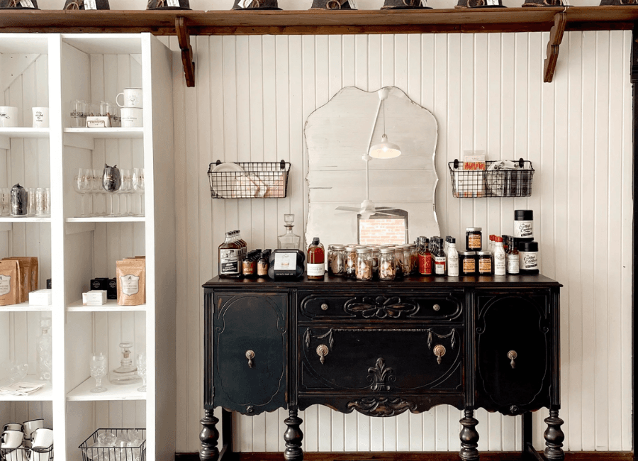 A vintage black dresser adorned with various jars and products, accompanied by a mirror and shelves displaying glassware.
