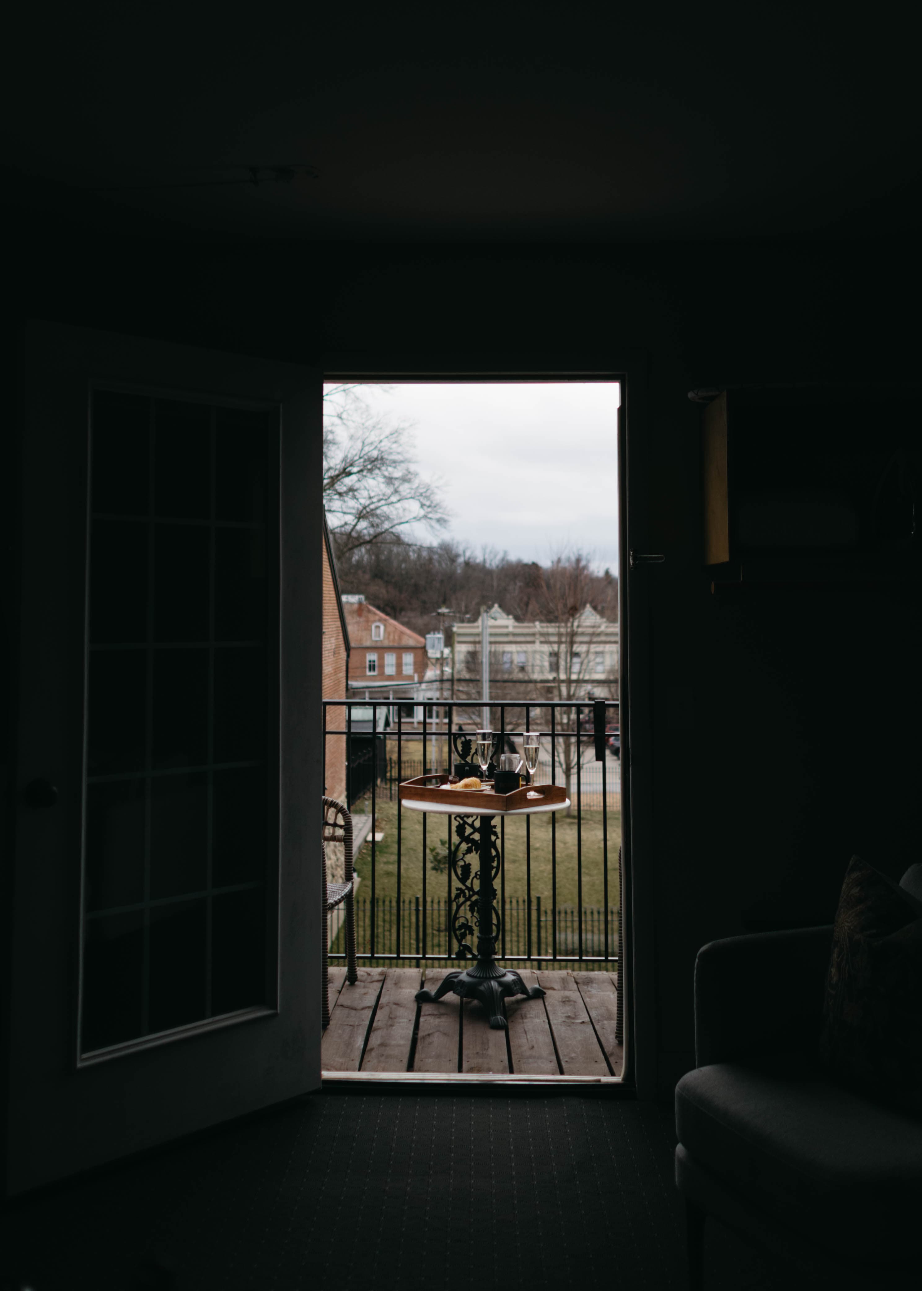 View of a balcony with a table set for two, framed by an open door.