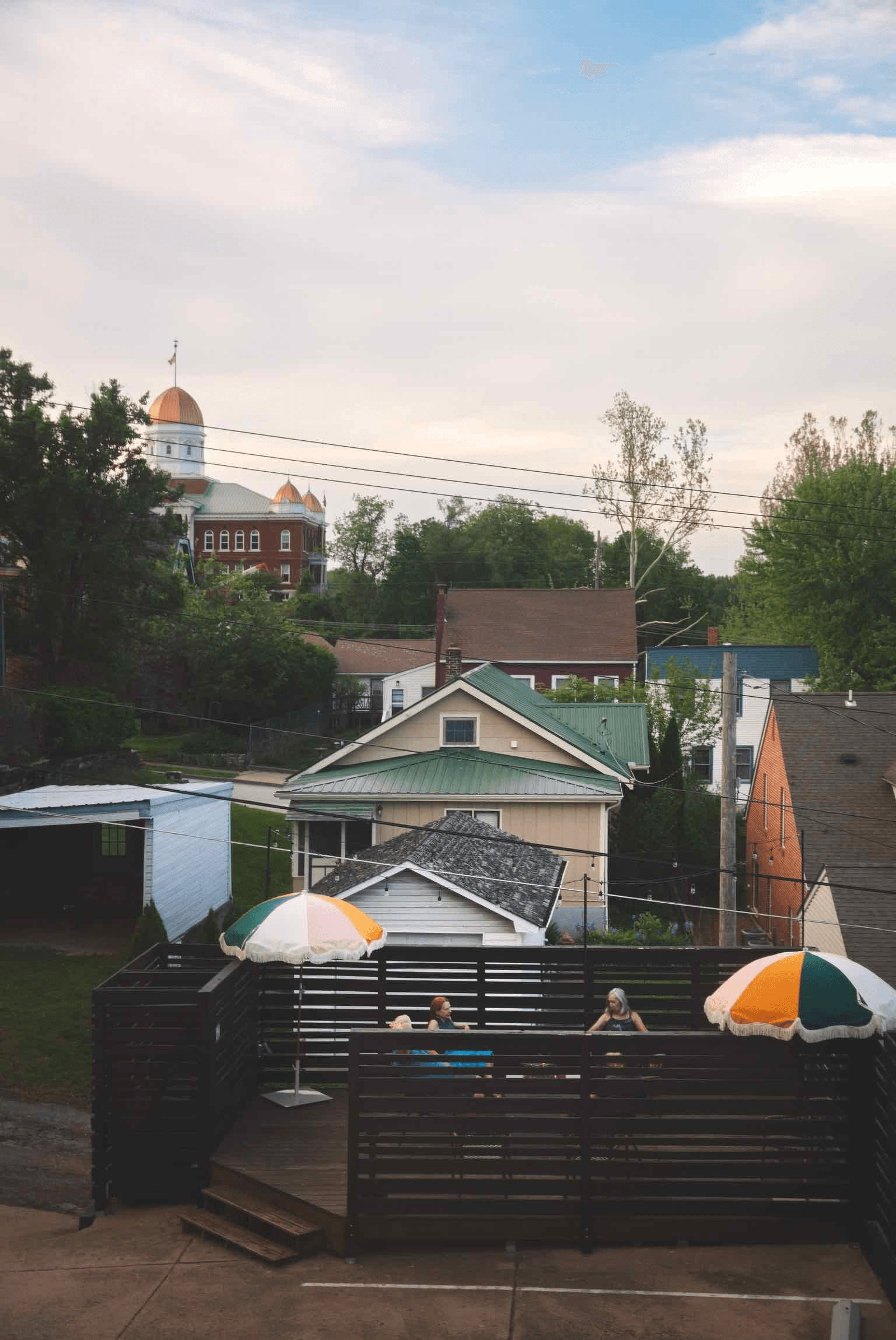 A view of a deck with two umbrellas, overlooking houses and a distant dome building under a cloudy sky.