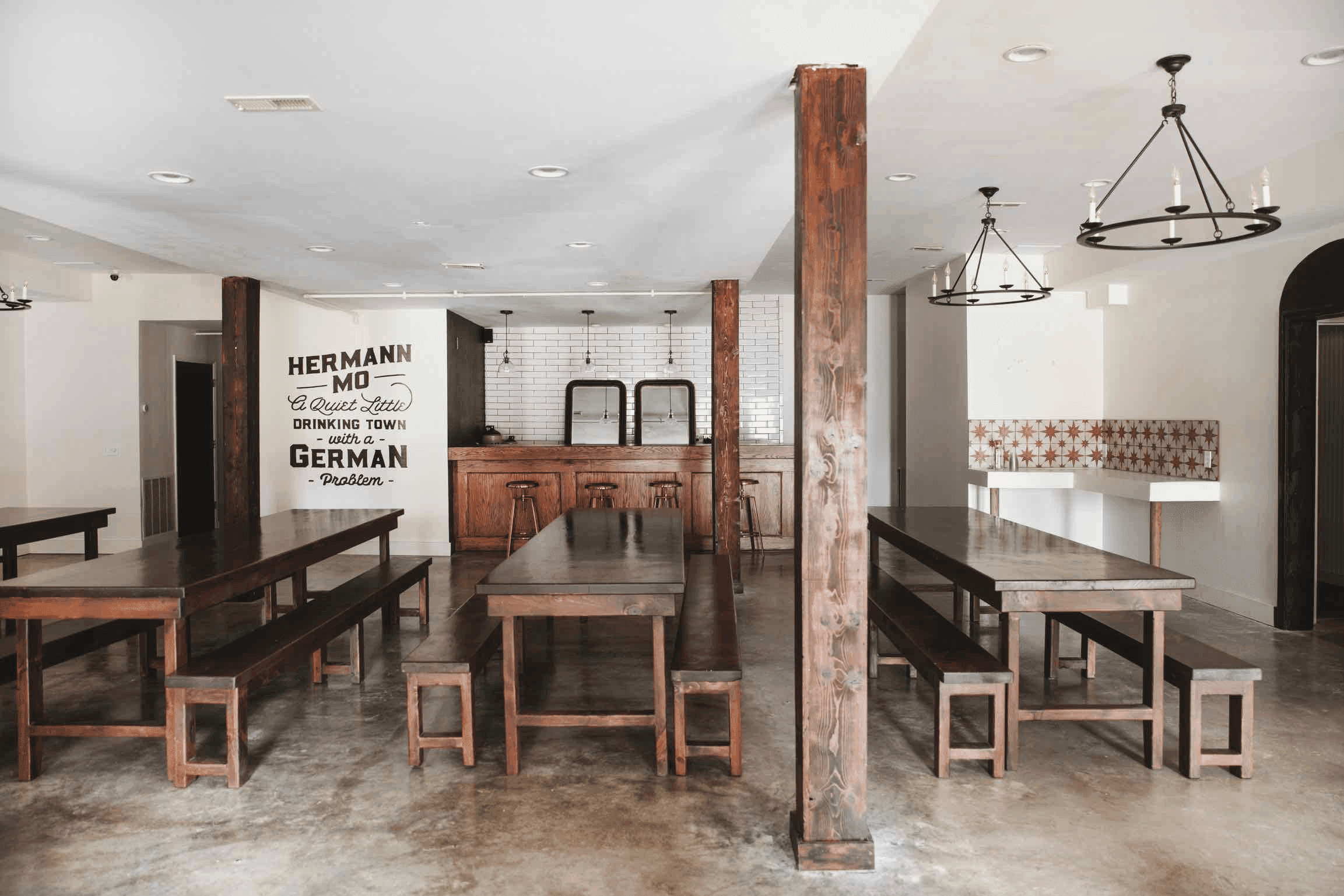Interior of a rustic dining area featuring wooden tables, benches, and a bar with a white tiled backsplash.