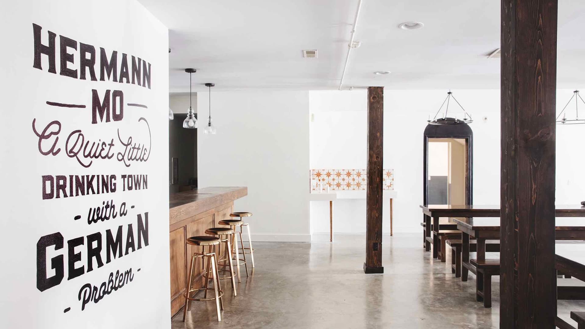 Interior of a stylish bar featuring a wall with the text "Hermann MO A Quiet Little Drinking Town with a German Problem."