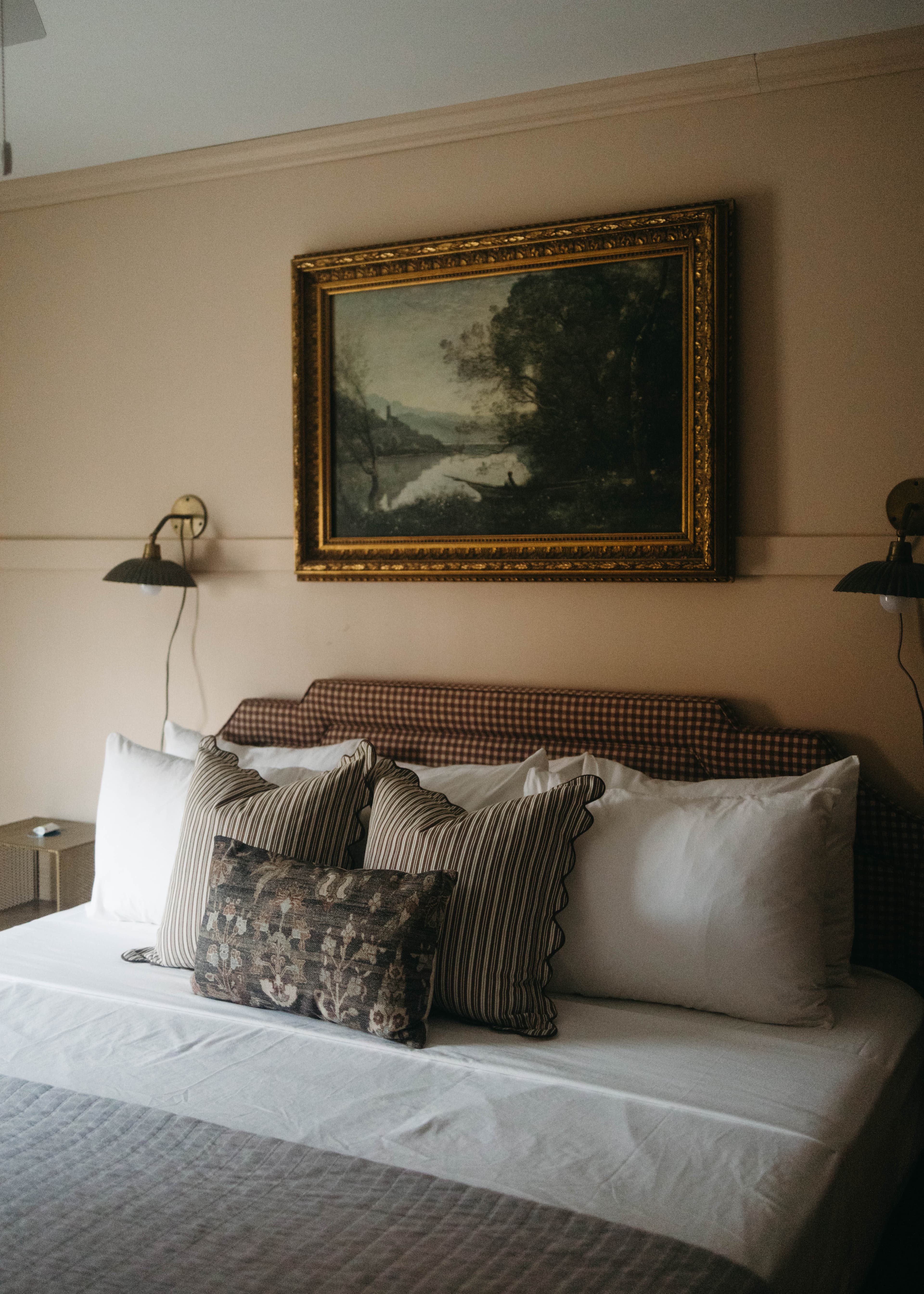 A cozy bedroom featuring a bed with decorative pillows and a vintage painting above the headboard.