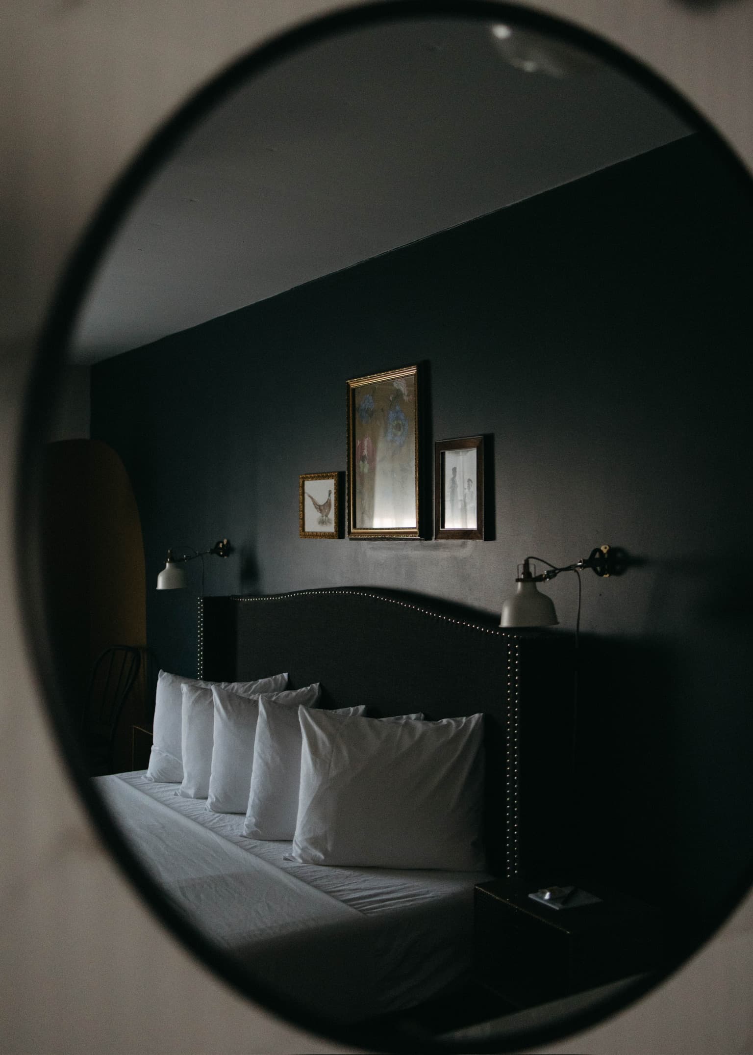 A reflection of a cozy hotel room featuring a bed with four white pillows and framed art on a dark wall.