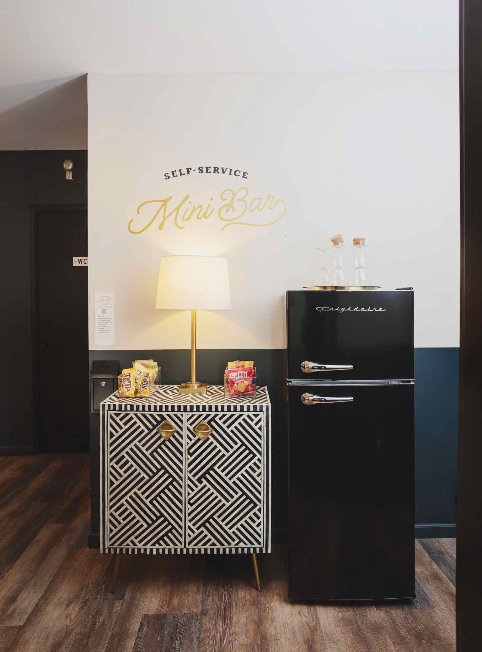 A stylish mini bar setup featuring a black fridge, patterned cabinet, and lamp against a modern wall.