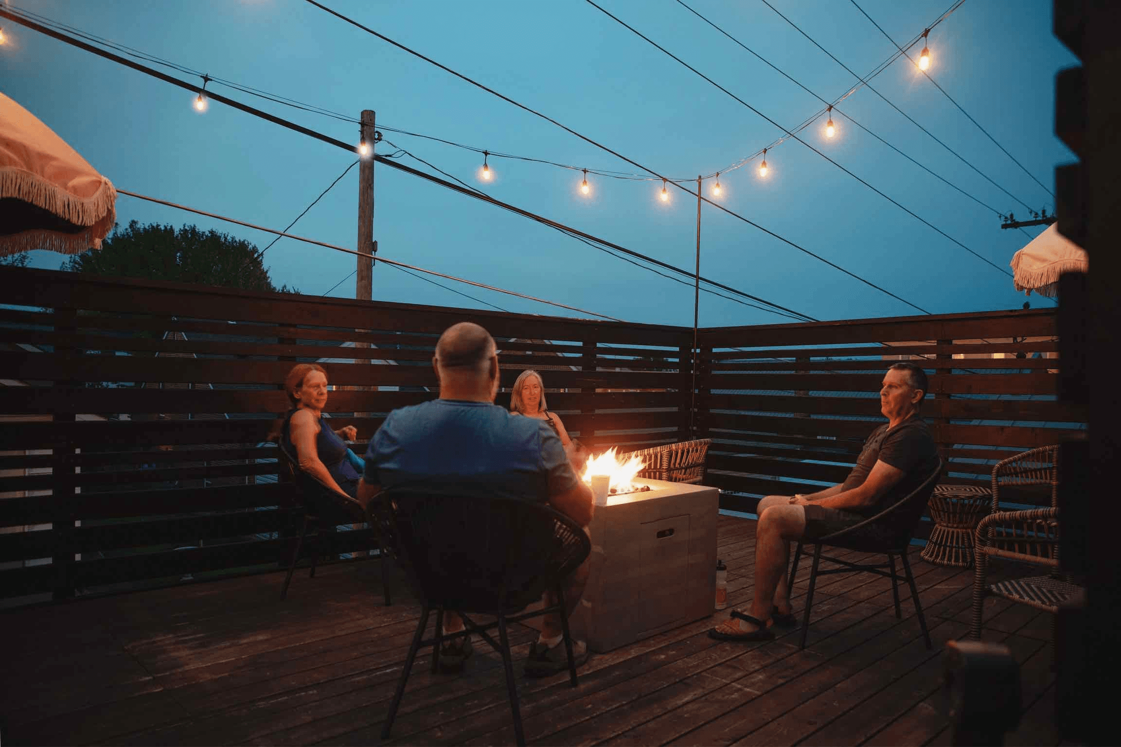 Four people sit around a fire pit on a dimly lit patio.