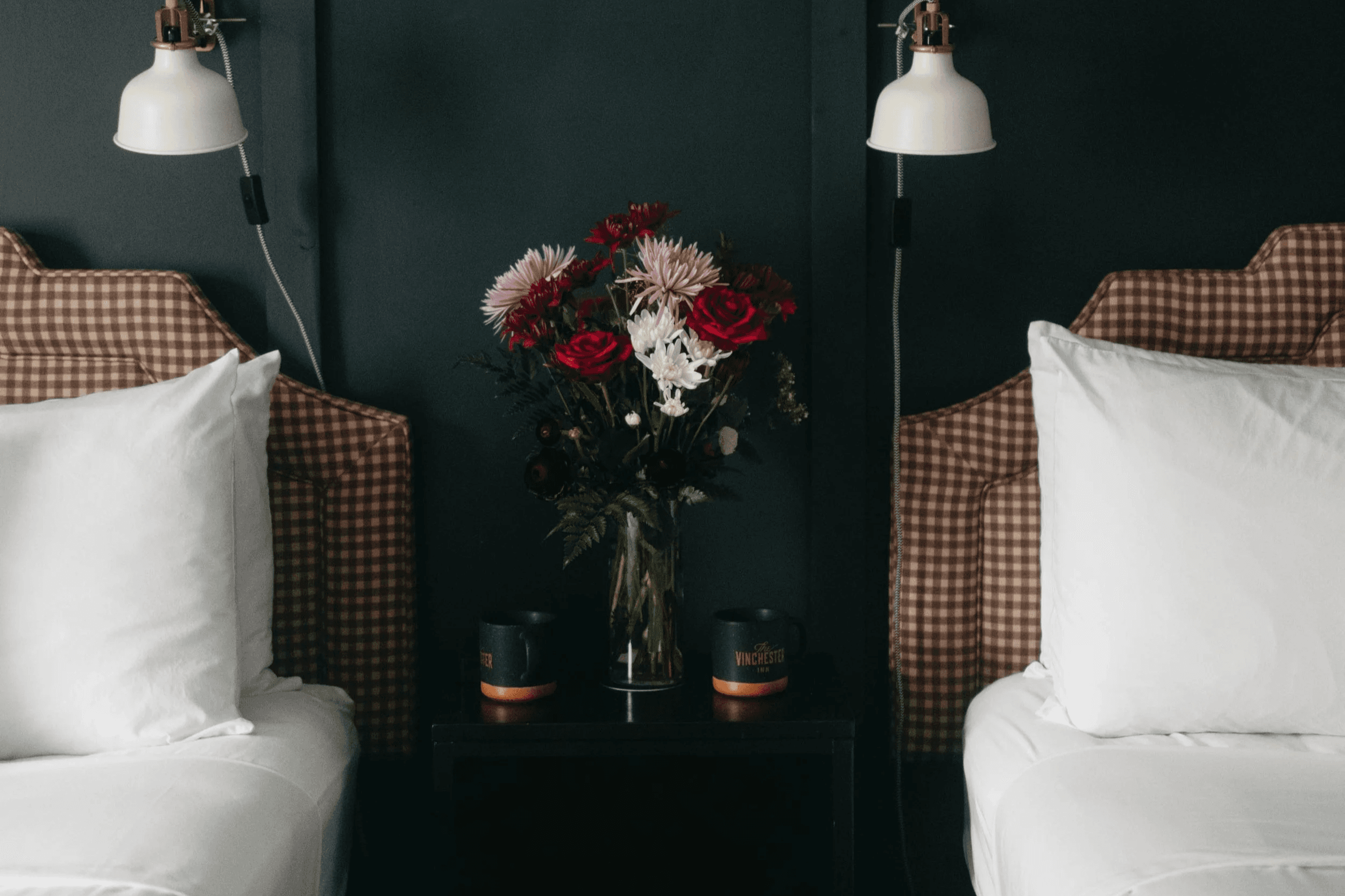 A vase of colorful flowers sits between two neatly made beds with patterned headboards and bedside lamps.