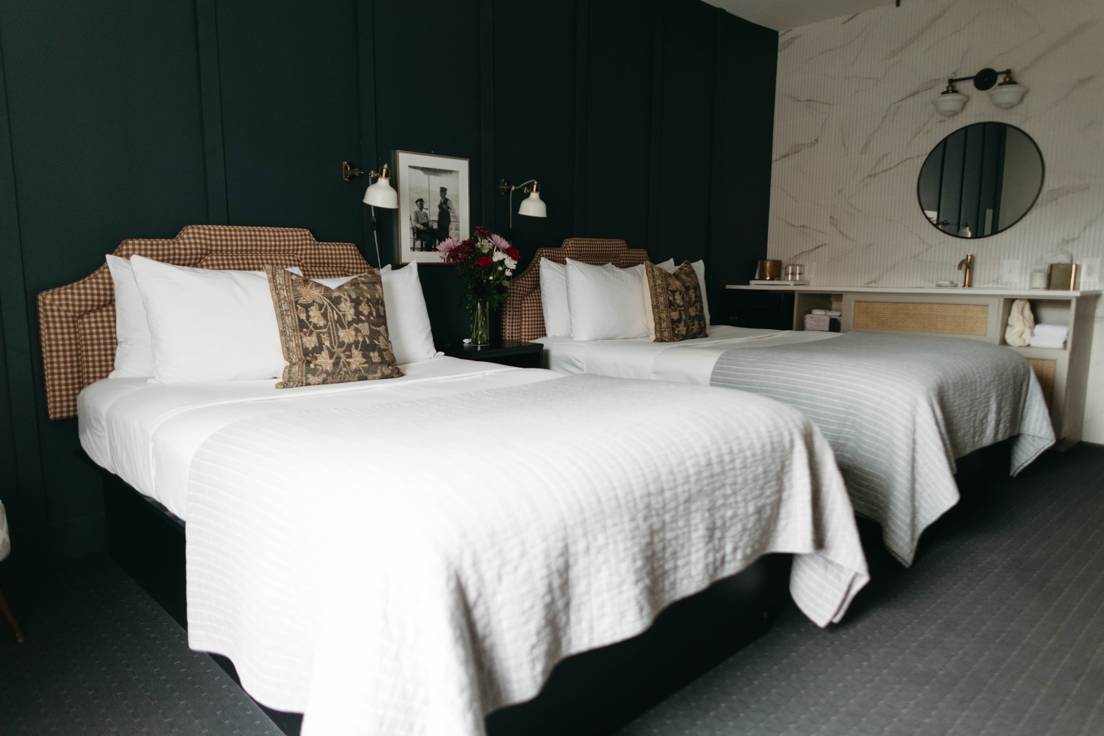 A stylish hotel room featuring two beds with patterned headboards and dark green walls.
