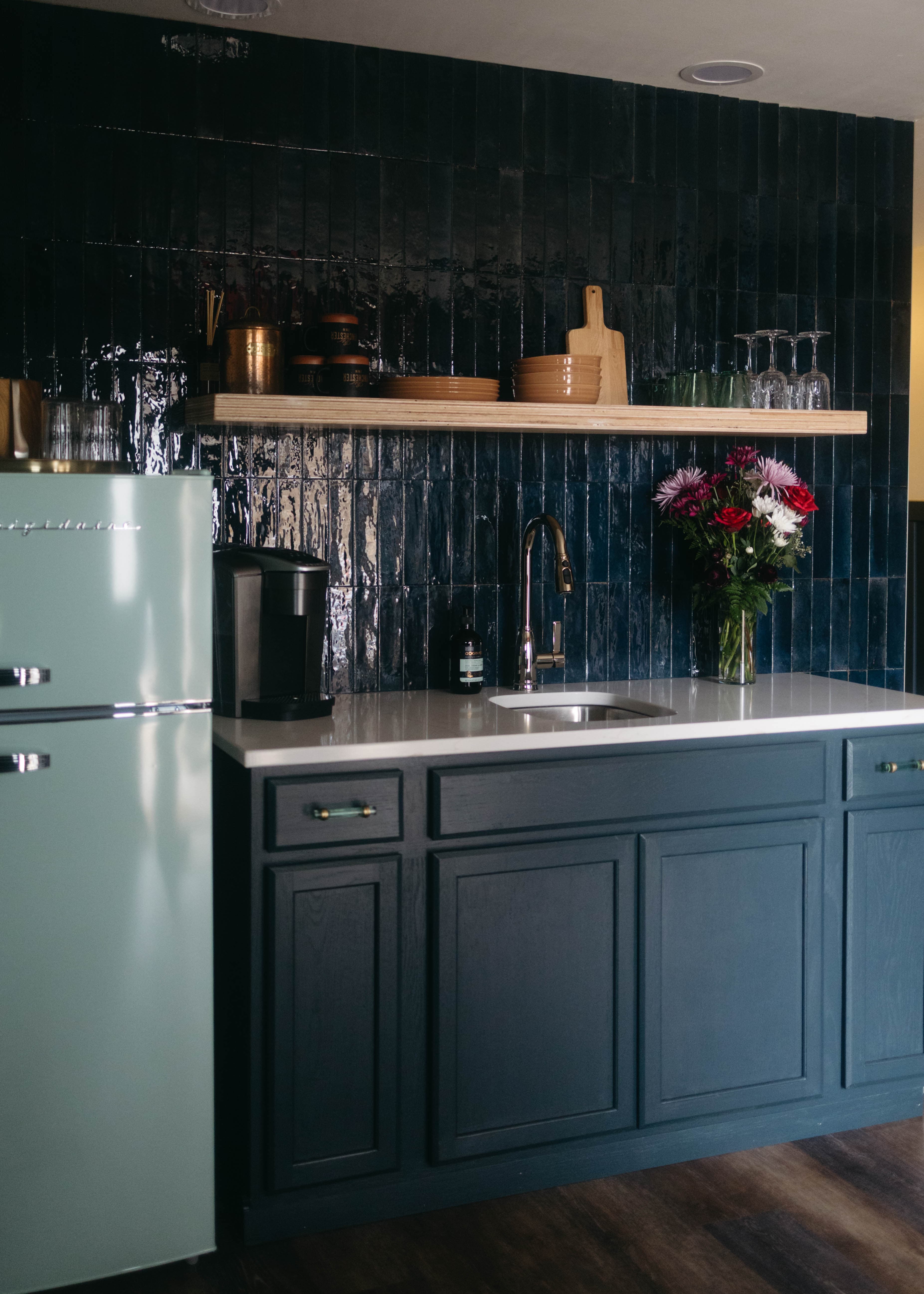 A modern kitchen featuring a vintage mint green refrigerator, dark cabinetry, and a wooden shelf with decorative items and flowers.